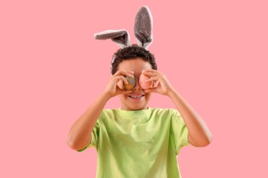 African-American little boy in bunny ears with Easter eggs on pink background