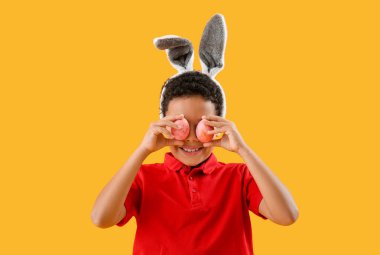 African-American little boy in bunny ears with Easter eggs on yellow background