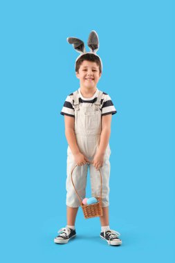 Cute little boy with bunny ears and Easter basket on light blue background