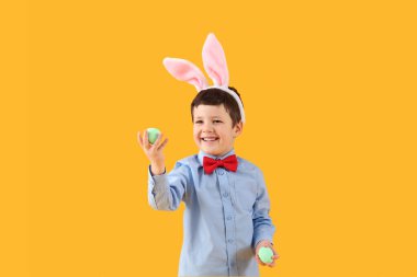 Cute little boy with bunny ears and Easter eggs on yellow background