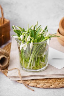 Glass with beautiful snowdrops on grey table