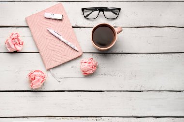 Composition with notebook, cup of coffee, eyeglasses, pen and crumpled paper balls on light wooden background
