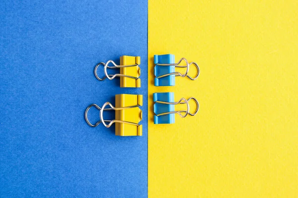 Blue and yellow binder clips on color background