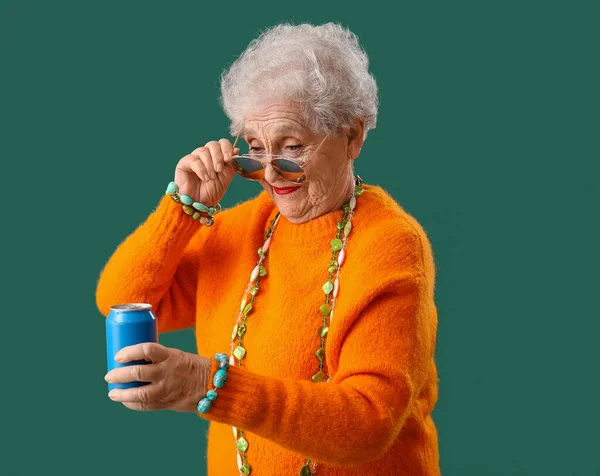 Senior woman in sunglasses with can of soda on green background