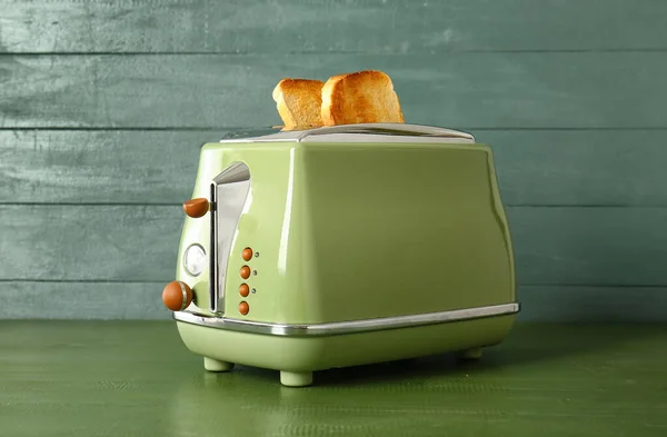 Modern toaster with crispy bread slices on green wooden table