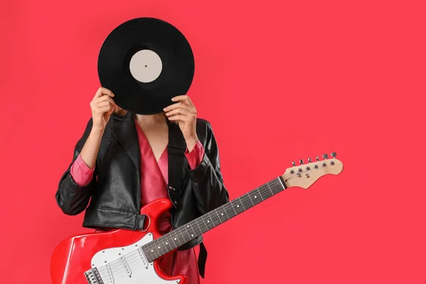 Young woman with vinyl disk and guitar on red background