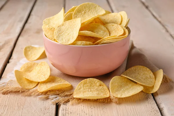 Bowl with delicious potato chips on white wooden background