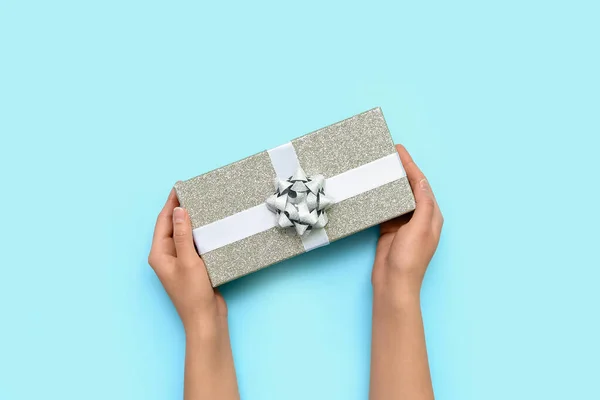 Female hands and gift box with white bow on blue background