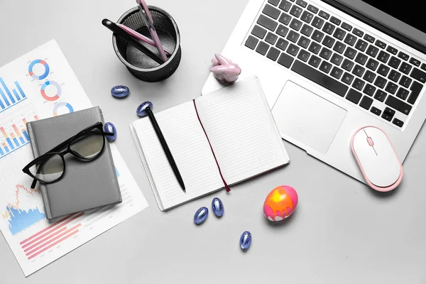Blank notebooks with office stationery, laptop and Easter eggs on grey background