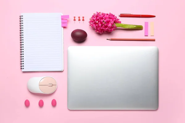 Laptop with office stationery, flower and Easter eggs on pink background