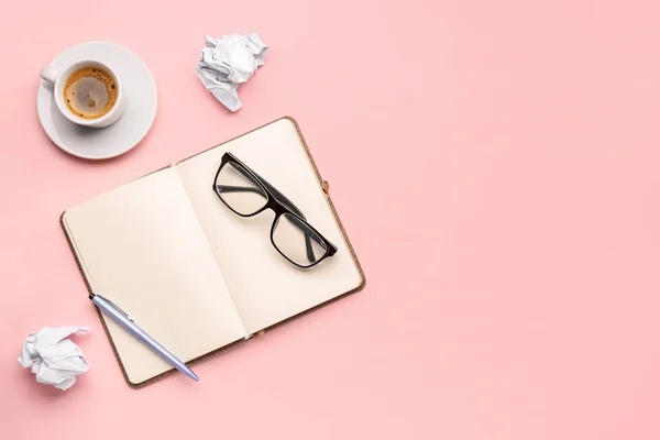 Composition with notebook, eyeglasses, crumpled paper balls and cup of coffee on pink background