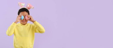 Tavşan kulaklı küçük Afro-Amerikalı çocuk ve eflatun arkaplanlı paskalya yumurtaları.