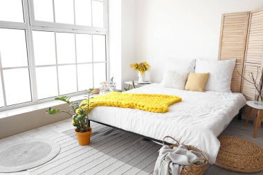 Modern yatak odasının içinde vazo ve penceresinde mimoza çiçekleri var.