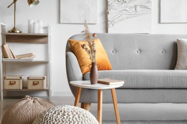 Kuru kamışlı vazo, masada kitap ve oturma odasında puf.