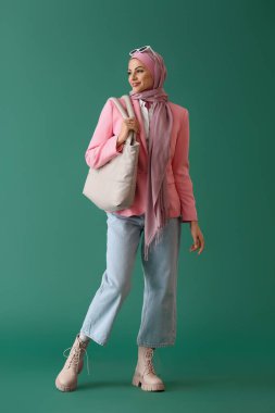 Yeşil arka planda çantası olan pembe tesettürlü şık Müslüman kadın