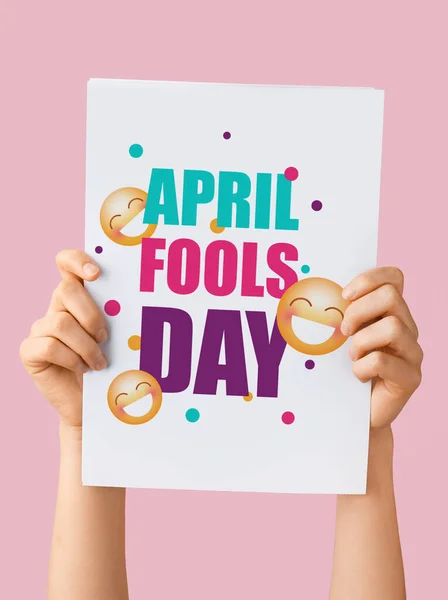 Female hands holding poster with text APRIL FOOLS DAY on pink background