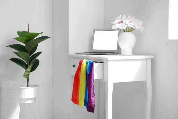 Workplace with laptop, flowers in vase and LGBT flag near light wall