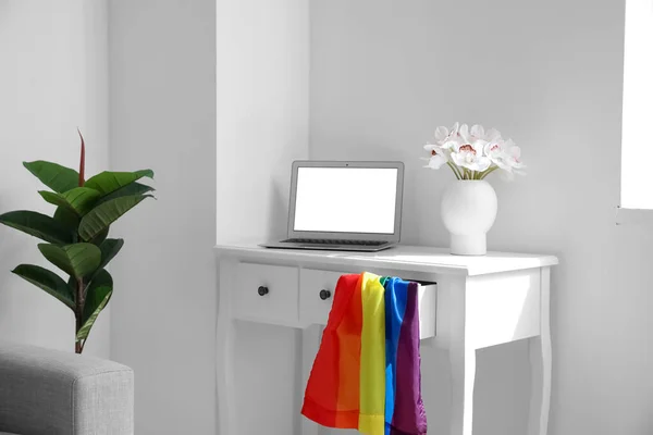 Workplace with laptop, flowers in vase and LGBT flag near light wall