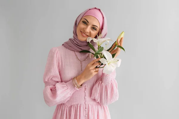 軽い背景にユリの花を持つスタイリッシュなイスラム教徒の女性 — ストック写真
