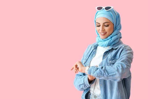 ピンクの背景に腕時計を見てスタイリッシュなイスラム教徒の女性 — ストック写真