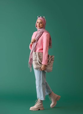 Yeşil arka planda çantası olan pembe tesettürlü şık Müslüman kadın