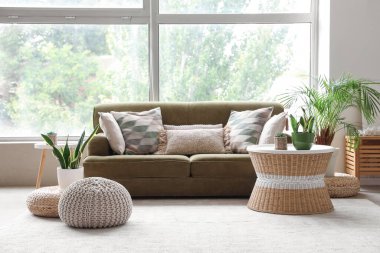 Yeşil kanepeli, puflu ve çiçekli rahat bir oturma odası.