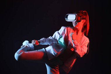 Pretty young woman in VR glasses training on black background