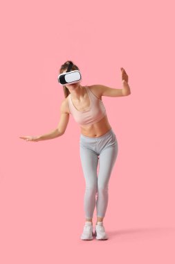 Pretty young woman in VR glasses on pink background