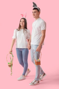 Happy young couple in bunny ears with baskets of Easter eggs on pink background