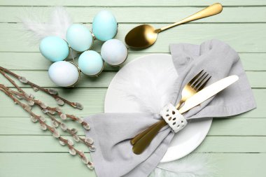 Table setting with Easter eggs, cutlery and pussy willow branches on green wooden background