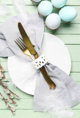 Table setting with Easter eggs, cutlery and pussy willow branches on green wooden background