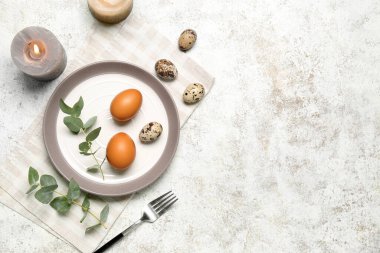 Paskalya yumurtaları, çatal ve beyaz grunge arka planında yanan mumlarla masa ayarı