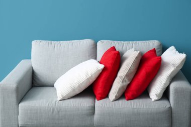 Stylish decorative pillows on cozy grey sofa near blue wall