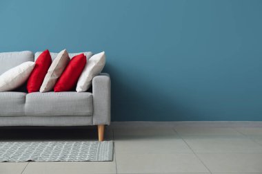 Stylish decorative pillows on cozy grey sofa near blue wall