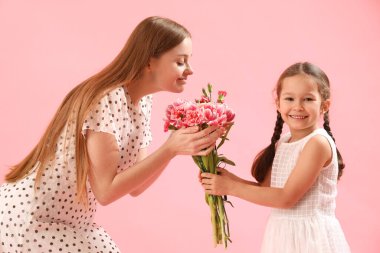 Sevimli küçük kız pembe arka planda çiçeklerle annesini selamlıyor.