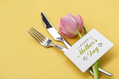 Mesajlı tebrik kartı Mutlu Anneler Günü, sarı arka planda çatal bıçak takımı ve lale çiçeği, yakın plan.