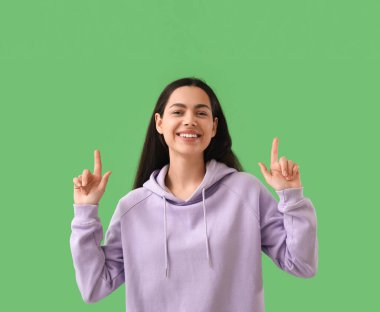 Güzel genç bayan yeşil arka plandaki bir şeyi işaret ediyor.