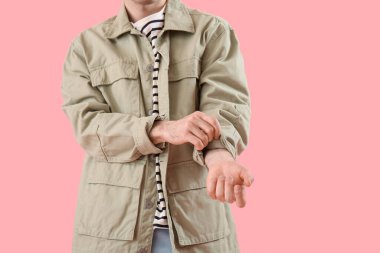 Young man rolling up his sleeve on pink background
