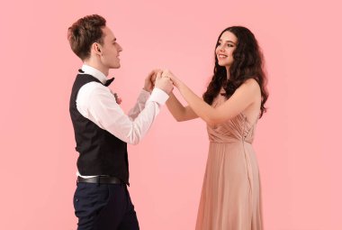 Beautiful couple dressed for prom dancing on pink background
