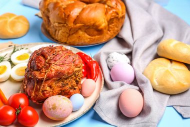 Tasty dishes for Easter dinner and beautiful painted eggs on color background, closeup