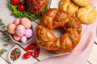 Tasty dishes and painted eggs for Easter dinner on light wooden background