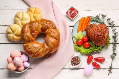 Tasty dishes and painted eggs for Easter dinner on light wooden background