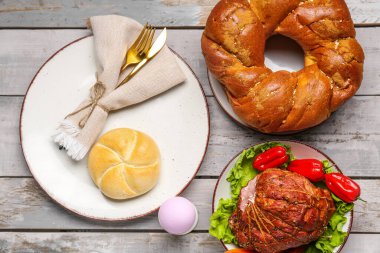Easter table setting with tasty ham and wreath bread on light wooden background