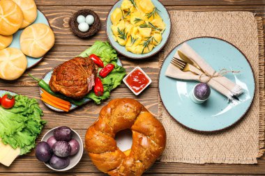 Tasty dishes and painted eggs for Easter dinner on wooden background