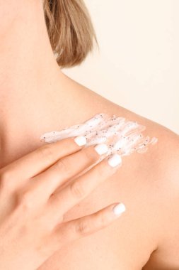 Woman applying scrub on her shoulder against color background, closeup