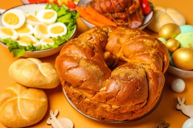 Tasty Easter wreath bread and dishes for dinner on color background, closeup