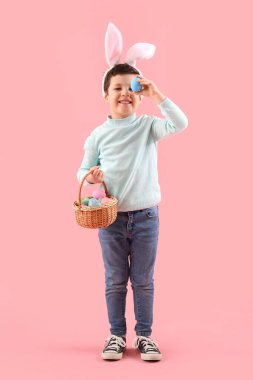 Cute little boy with bunny ears and Easter basket on pink background