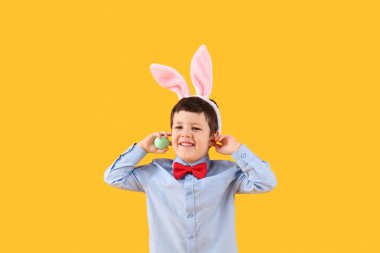 Cute little boy with bunny ears and Easter egg on yellow background