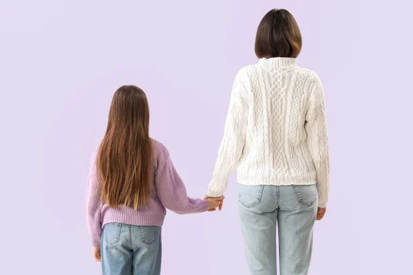 小女孩和她的妈妈穿着暖和的毛衣 手牵着紫丁香背景的手 回头看 — 图库照片
