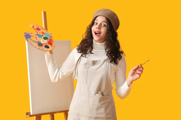 用画笔 画板和画架在黄色背景上的令人惊讶的青少年艺术家 — 图库照片